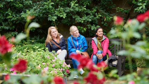 Visitors on a bench in the garden at East Riddlesden Hall, Yorkshire, on a rainy summer day, with red roses blooming in the forground